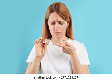 Upset Woman With Herpes Applying Cream On Lips Against Light Blue Background