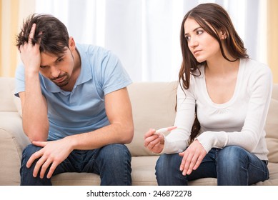 Upset woman is looking in pregnancy test. Frustrated man is sitting next to her.