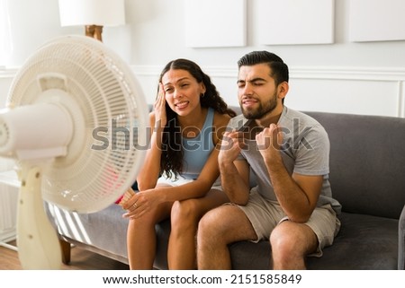 Upset woman and man sweating and feeling very hot during the hot weather. Young couple turning on the electric fan