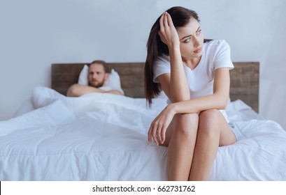 Upset Woman Sitting On Bed With Angry Husband Behind