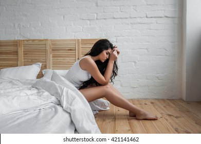 Upset Woman Sitting On Edge Of Bed In Bedroom