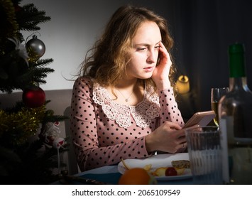 Upset Woman Sitting At Table Celebrating Holiday Alone And Using Phone At Christmas Night