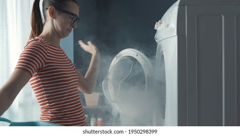 Verärgerte Frau, die ihre zerbrochene Waschmaschine anstarrt, ist das Zimmer voller Rauch