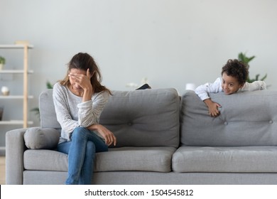 Upset Woman Suffering From Haughty African American Boy Bad Behavior, Mother Sitting On Couch, Hiding Face Under Palm, Little Noisy Son Climbing On Sofa, Frustrated Mum Tired Of Difficult Kid