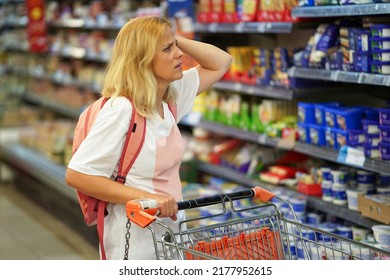 Upset woman in a supermarket with an empty shopping trolley. Crises, rising prices for goods and products. Woman looks shocked in a grocery supermarket price increase and inflation