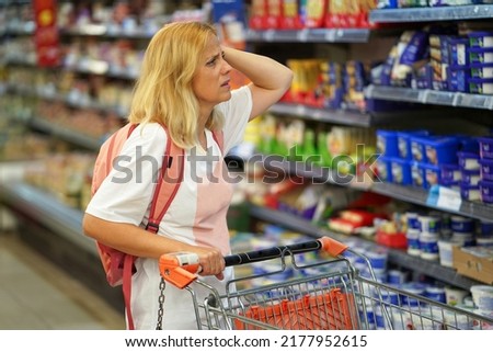 Upset woman in a supermarket with an empty shopping trolley. Crises, rising prices for goods and products. Woman looks shocked in a grocery supermarket price increase and inflation