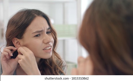 Upset woman taking off earrings from ear looking in mirror in home bathroom. Unhappy woman feeling pain while take off earring from ear in bathroom. Female ear piercing. Beauty fashion and style - Powered by Shutterstock