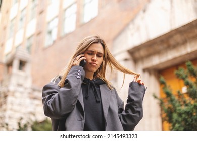 Upset Woman. Woman Talking Sad By The Bad News She Hear On The Cell Mobile Phone. Gloomy Girl Short Hair Wear Grey Suit And Twisting A Lock Of Hair On Her Finger.