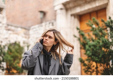 Upset Woman. Woman Talking Sad By The Bad News She Hear On The Cell Mobile Phone. Gloomy Girl Short Hair Wear Grey Suit And Twisting A Lock Of Hair On Her Finger.