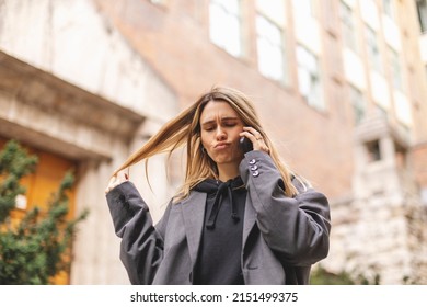 Upset Woman. Woman Talking Sad By The Bad News She Hear On The Cell Mobile Phone. Girl Short Hair Wear Grey Suit And Twisting A Lock Of Hair On Her Finger.