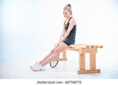 Upset Woman With Tennis Racket In Hands Sitting On Wooden Bench Isolated On White