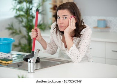 Upset Woman Using Plunger In Blocked Kitchen Sink