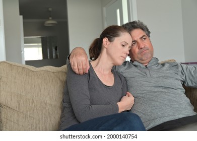 Upset Worried Couple (male Age 40-50 And Female Age 30-40) Sitting On A Couch Alone With Puzzled Face Expression In Home Living Room.Real People. Copy Space