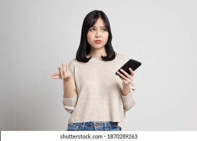 Upset young asian woman holding smartphone standing on isolated white background. She was very stressed and depressed. - Powered by Shutterstock