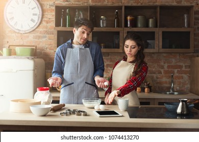 Upset Young Couple Baking Pie And Having Problems In Loft Kitchen. Young Family Cooking At Home, Using Digital Tablet. Mockup For Recipe