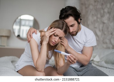 Upset young husband comforting his depressed young wife with negative pregnancy test on bed at home. Millennial couple cannot have baby, suffering from infertility indoors - Powered by Shutterstock