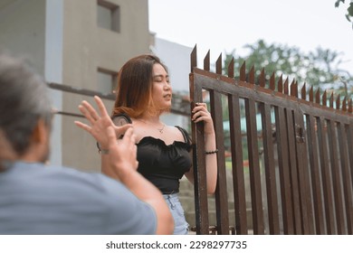 An upset young lady refuses to listen to her apologetic boyfriend's alibis and excuses. Denying him entry into their home. Breakup scenario of a live-in couple. - Shutterstock ID 2298297735