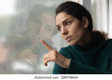 Upset young Latino woman look in window distance feel depressed unhappy alone at home. Sad stressed millennial Hispanic female on lockdown indoors, lack communication. Solitude, loneliness concept.