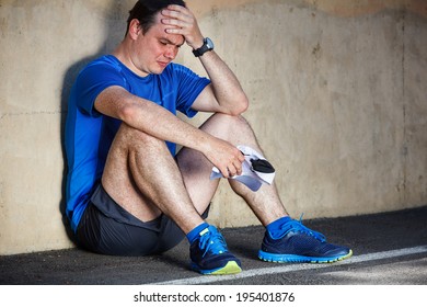 Upset Young Male Runner Resting Leaning Against Wall.