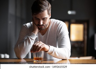 Upset young man drinker alcoholic sitting at bar counter with glass drinking whiskey alone, sad depressed addicted drunk guy having problem suffer from alcohol addiction abuse, alcoholism concept