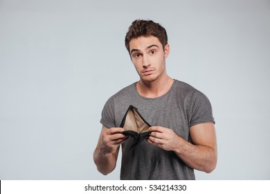 Upset young man holding empty wallet over white background
