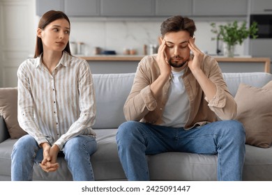 Upset young man touching head, showing signs of stress, while concerned woman looking at husband, highlighting relationship tension - Powered by Shutterstock