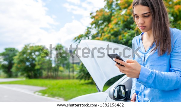 Upset young woman\
with cell phone near broken car . Young woman using mobile phone\
while looking at broken down car on street. Young woman with broken\
car calling for help 