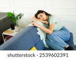 Upset young woman feeling lonely and depressed while sitting on a sofa at home and holding a smartphone