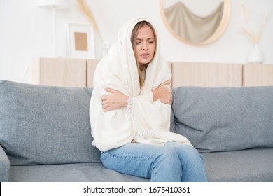 Upset Young Woman Freezing, Feeling Cold At Home, Sitting On Sofa Covered With Blanket 