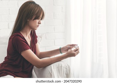 Upset Young Woman Holding Positive Test Pregnancy In Own Hand Worried Something Unwanted Life While Sitting On White Sofa Beside Windows At Home.