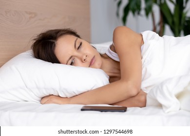 Upset young woman lying on bed looking at phone waiting for mobile call message feeling worried sad hurt jealous, heartbroken lonely teen girl anxious ignored by boyfriend not texting on cellphone
