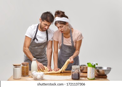 Upset Young Woman And Man Knead Dough Without Rolling Pin, Feel Tired Of Long Hours Cooking At Kitchen, Have No Inspiration For Preparing Homemade Pastry, Being Dirty With Flour, Pose Near Table