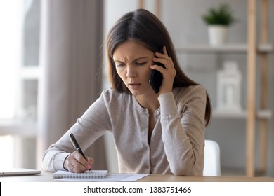 Upset young woman sit at office desk talking over phone disappointed hear bad news, sad pensive girl writing take notes in notebook feel unhappy speaking having unpleasant cellphone conversation - Powered by Shutterstock