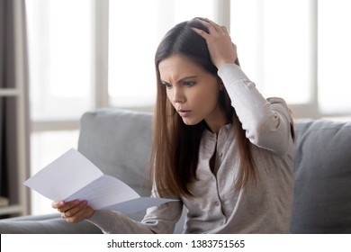 Upset young woman sit on couch scratch head shocked by unexpected negative news read in letter, disappointed girl surprised look at paper have bank debt, frustrated female get eviction notice
