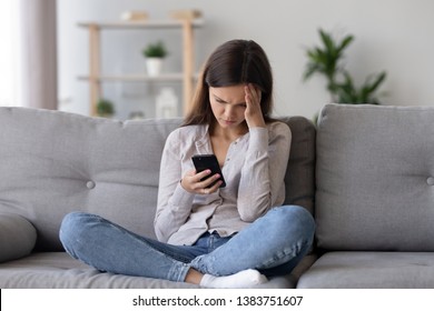 Upset Young Woman Sit On Couch At Home Hold Smartphone Receive Unpleasant Breakup Text Message, Sad Teen Girl On Sofa Feel Down Read Bad News On Cellphone Online, Think Of Problem Solution