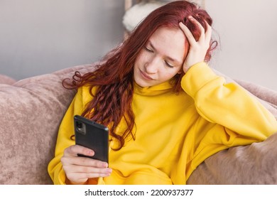 Upset Young Woman Sit On Couch At Home Hold Smartphone Receive Unpleasant Breakup Text Message, Sad Teen Girl On Sofa Feel Down Read Bad News On Cellphone Online, Think Of Problem Solution
