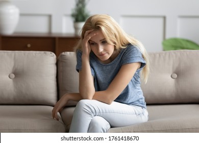Upset young woman sitting on couch looks unhappy, thinking about problems life troubles, break up and personal failure. Teenager suffers for unrequited first love, unsure girl, low self-esteem concept