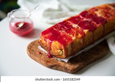 Upside Down Blood Orange Pound Cake On Olive Tree Board And Glass With Sauce On White Wooden Table