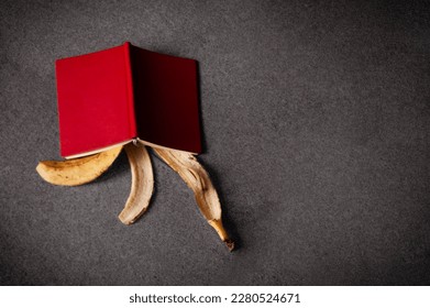 an upside down book with a red cover lies on a banana peel on the sidewalk - Powered by Shutterstock