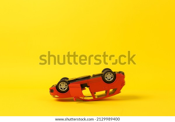 Upside down model of a toy car on a yellow\
background. Car accident