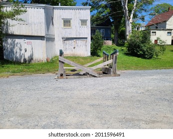 An Upside Down, Overturned Picnic Table. The Table Is Made Of Wood That Has Weathered And Grayed. The Bottom Pieces Of The Furniture Are Covered In A Green Plastic For Protection.