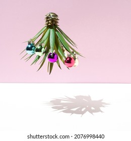 Upside down pineapple palm tree decorated with ornaments of balls of different colors and its shadow. Minimal Christmas concept on a pink white background