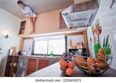 Upside Down Room. Young Woman Sitting On The Ceiling Of A Kitchen.