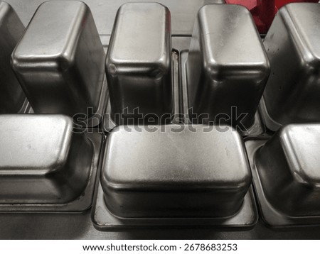 Upside down stainless containers arranged in a grid after washing. Clean industrial kitchen detail for storage, catering gear, and food service operations.