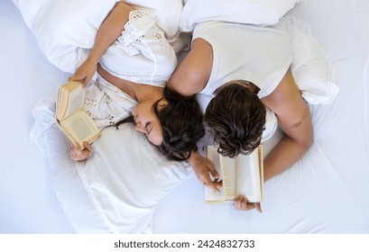 Upside down top view of an romantic, attractive, contented, young, sexy couple, man and woman, sunday morning in white bed, together reading books in nightwear, copy space