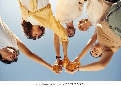 Upside down. View from below of people that are cheering with beer bottles.