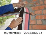 Upvc window installation. A man is installing a self adhesive rubber window seal strip, foam tape, or weather strip to a window frame to windproof and soundproof the window. 