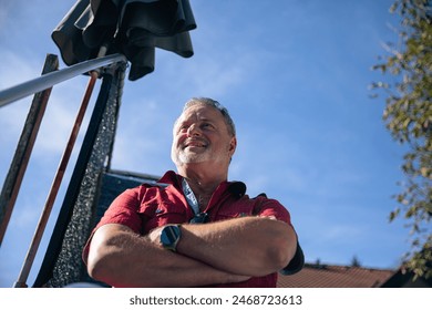 Upward angle of a thoughtful senior man gazing skyward, arms crossed in a pose of reflection - Powered by Shutterstock