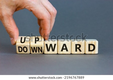 Upward or downward symbol. Businessman turns wooden cubes and changes the word 'downward' to 'upward'. Beautiful grey table, grey background. Business, upward or downward concept. Copy space.
