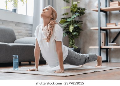 Upward facing dog yoga position. Mature Caucasian woman athlete yogi stretching her body, doing training yoga exercises for muscles to make her body fit and flexible at home - Powered by Shutterstock